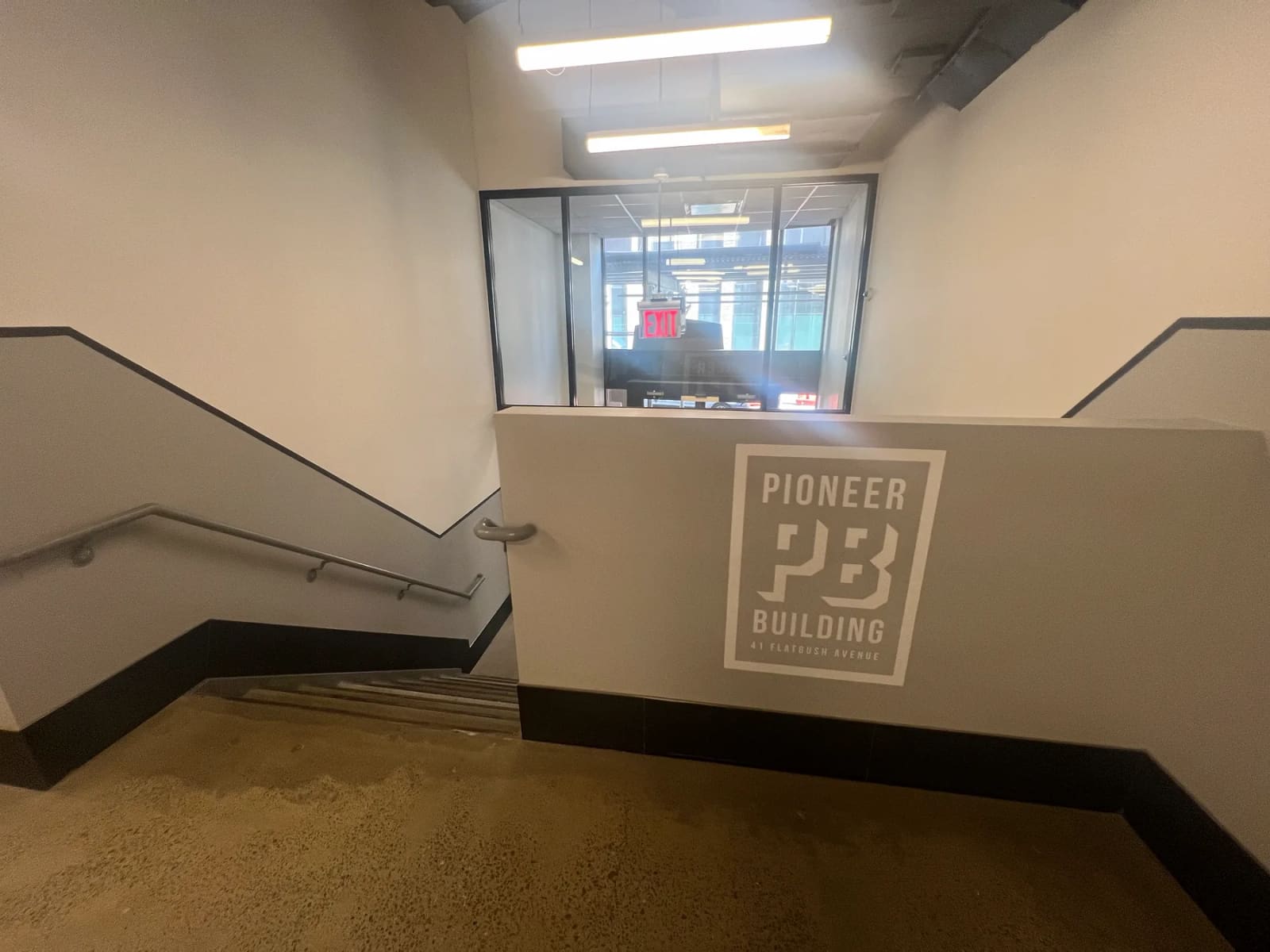 Pioneer Building sign displaying 41 Flatbush Avenue beside an interior staircase.
